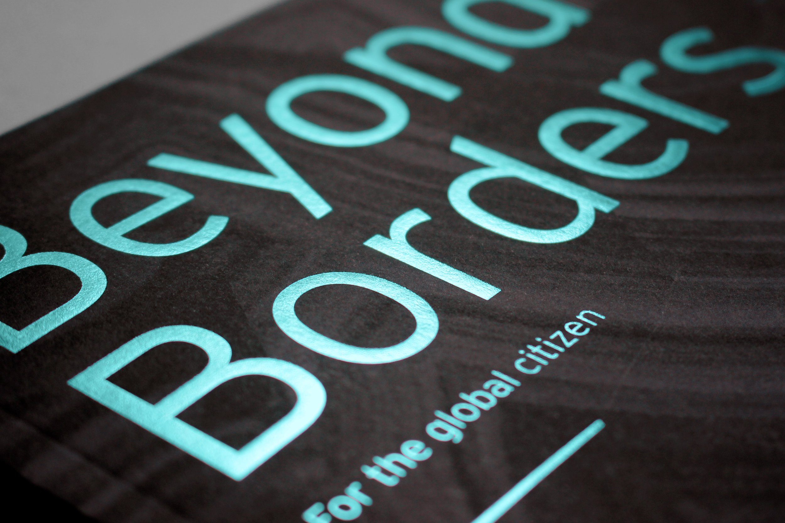 Beyond Borders cover macro: bright mint-green foil typography on matte dark brown stock